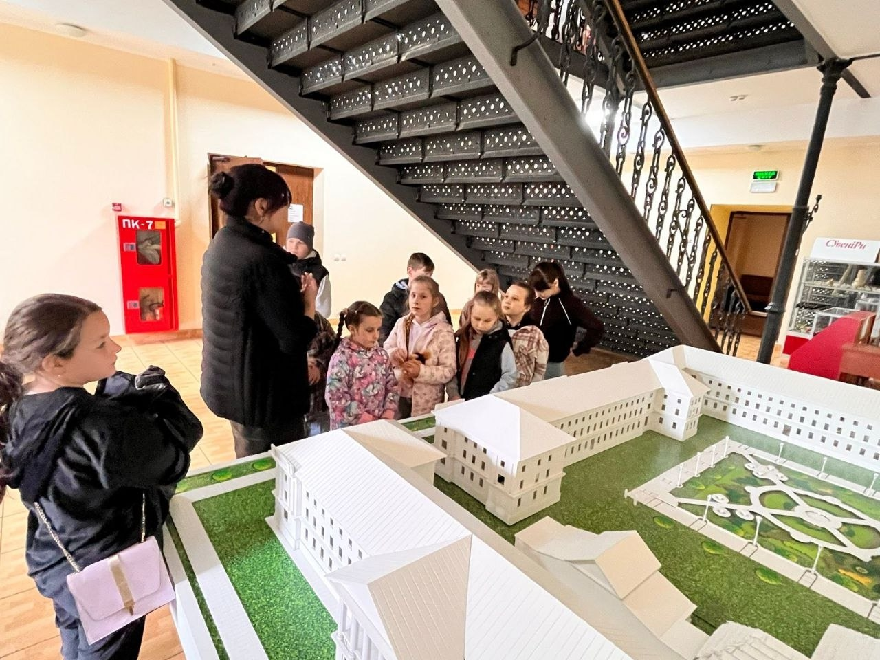 Група дітей та дорослий розглядають деталізований білий архітектурний макет великої будівлі.