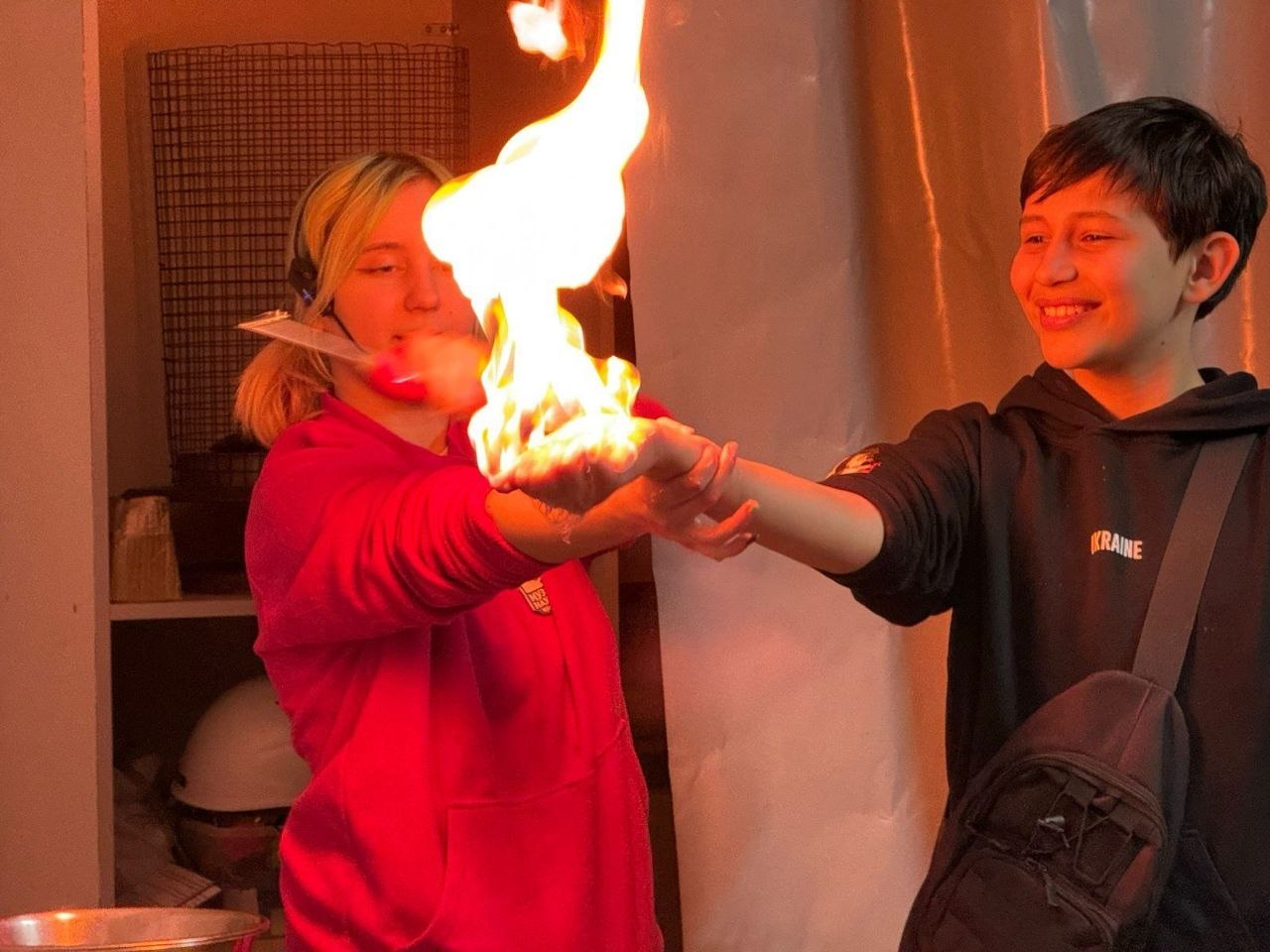 Дівчина-підліток та хлопчик шкільного віку демонструють науковий дослід із «палаючими руками», тримаючи яскраве полум'я на долонях у приміщенні.