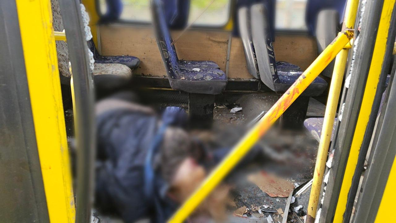 Інтер’єр жовтого автобуса з пошкодженими сидіннями та уламками на підлозі. У центрі кадру знаходиться заретушоване тіло людини.