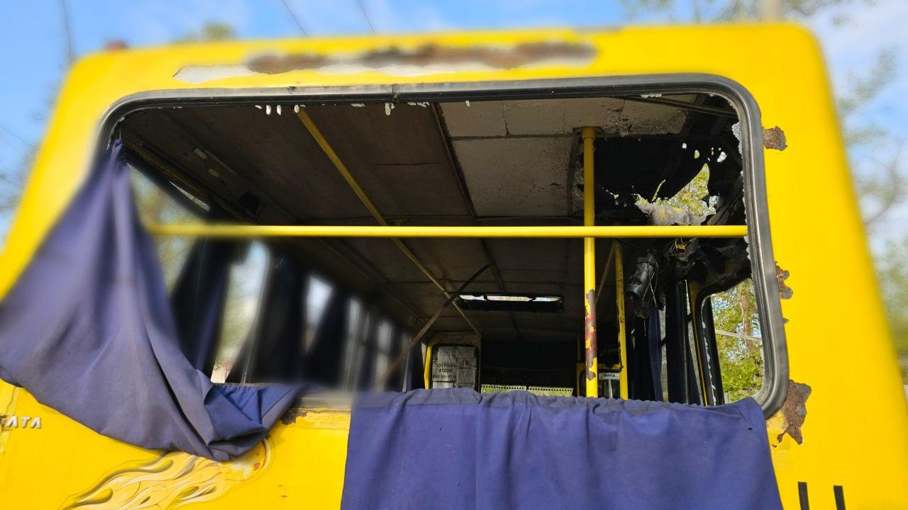 Задня частина жовтого автобуса з повністю вибитим склом. Через отвір видно пошкоджений салон із жовтими поручнями, обірвану обшивку стелі та сині шторки, що звисають з рами.