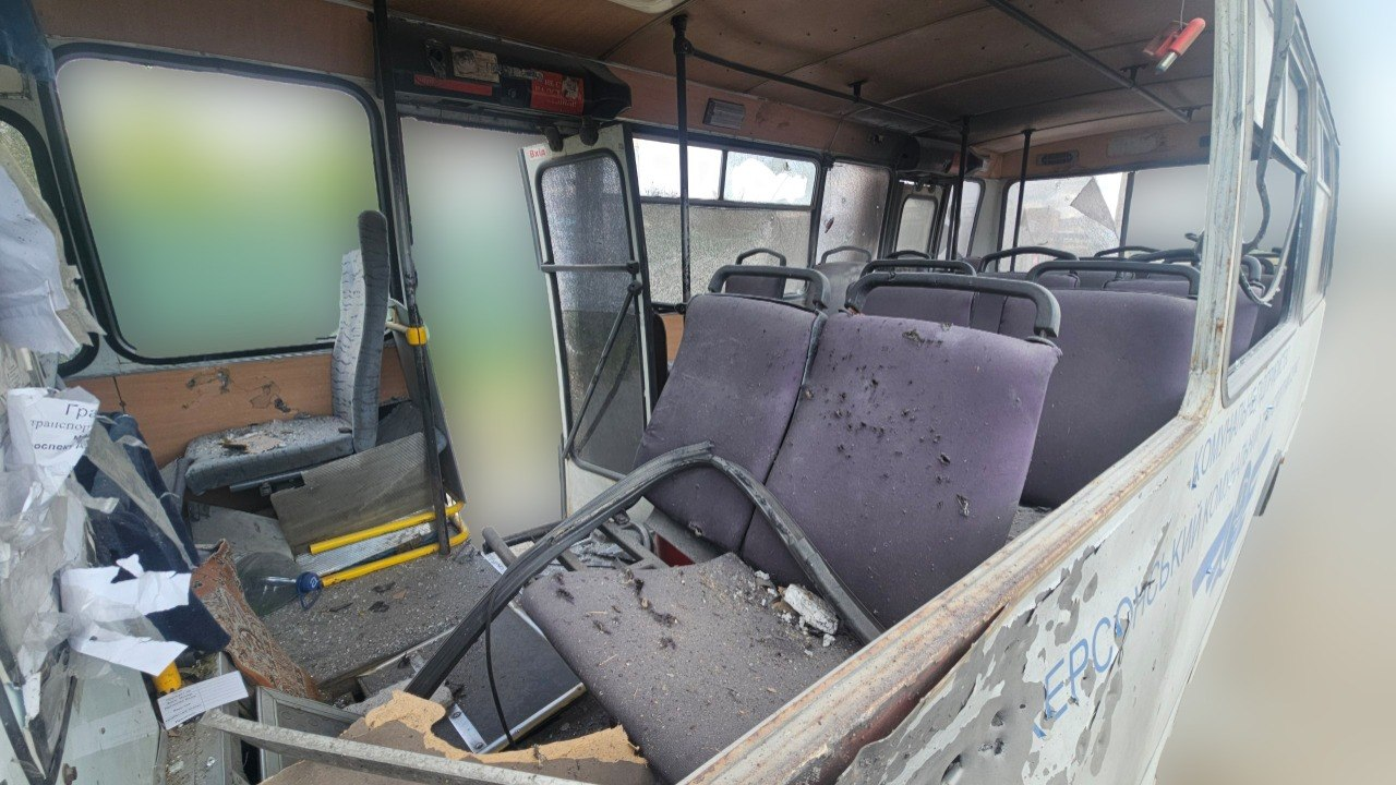 Пошкоджений салон білого автобуса з розбитими вікнами та посіченими уламками сидіннями. На підлозі та кріслах видно сміття, а кузов транспортного засобу має численні пробоїни.