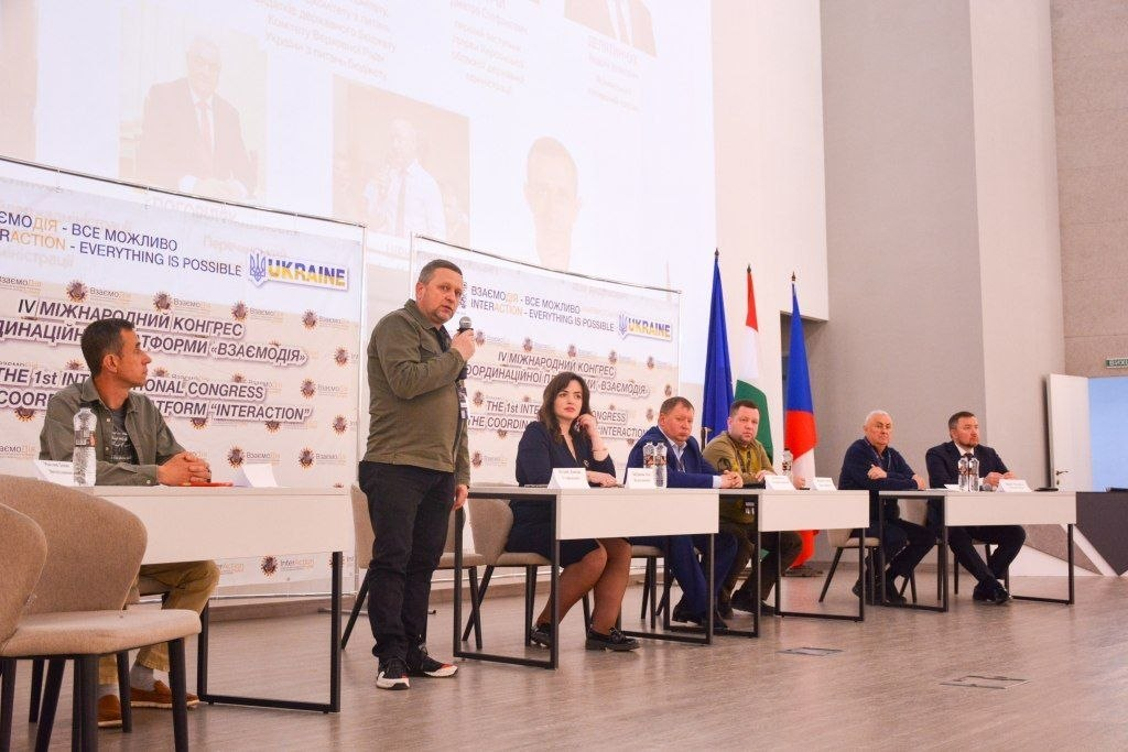 Спікер виступає з мікрофоном на офіційному заході на фоні банерів IV Міжнародного конгресу «Взаємодія» та державних прапорів.