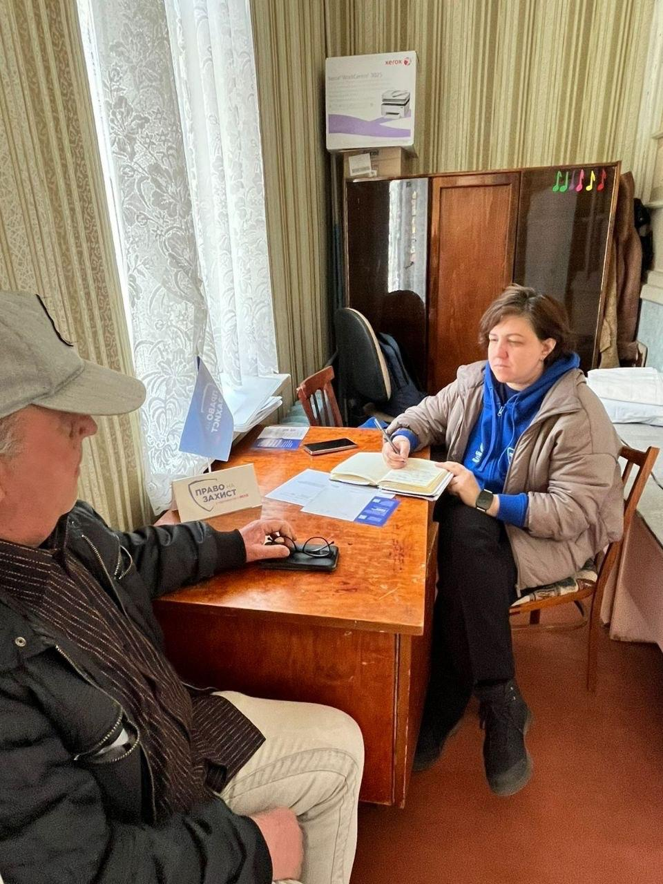 Представниця організації «Право на захист» веде прийом чоловіка за робочим столом у кабінеті, роблячи записи в блокноті.