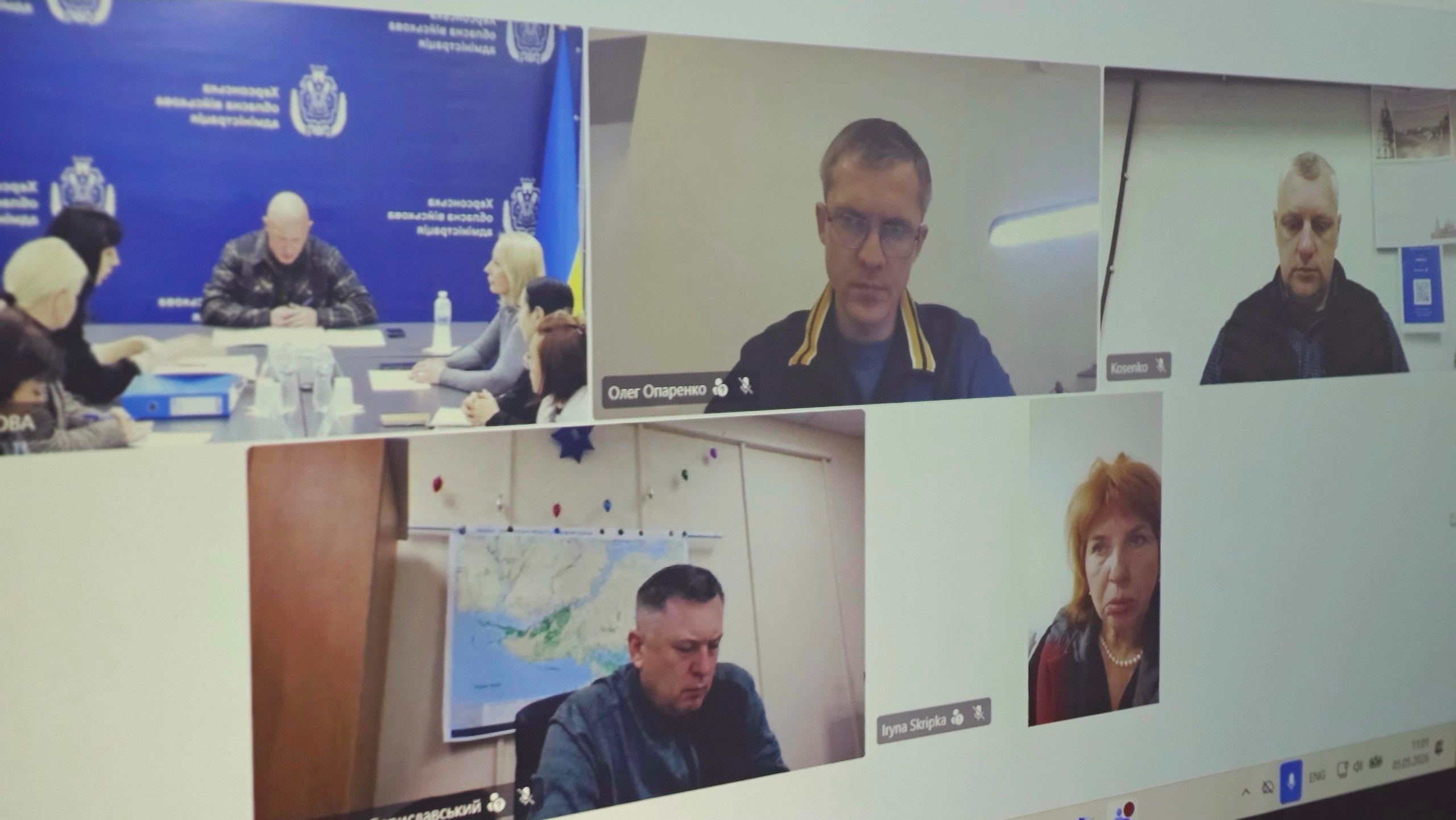 Екран монітора з вікнами відеоконференції, на яких зображені учасники офіційної онлайн-зустрічі. В одному з вікон видно групу людей за столом на фоні синього банера, в інших — окремі особи на фоні робочих кабінетів.