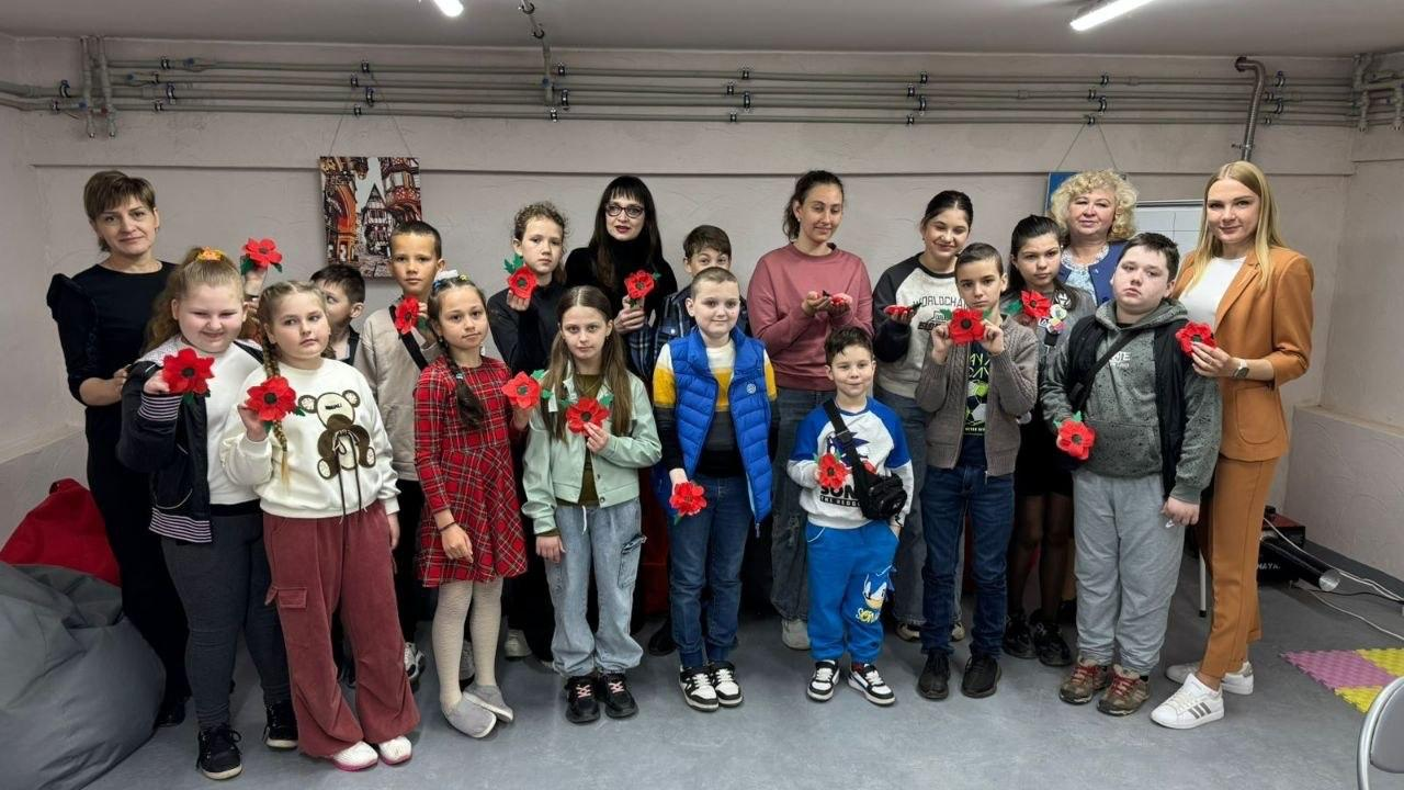 Групова фотографія дітей та дорослих у приміщенні. Учасники тримають у руках червоні маки, виготовлені власноруч під час тематичного майстер-класу до Дня пам'яті та примирення.