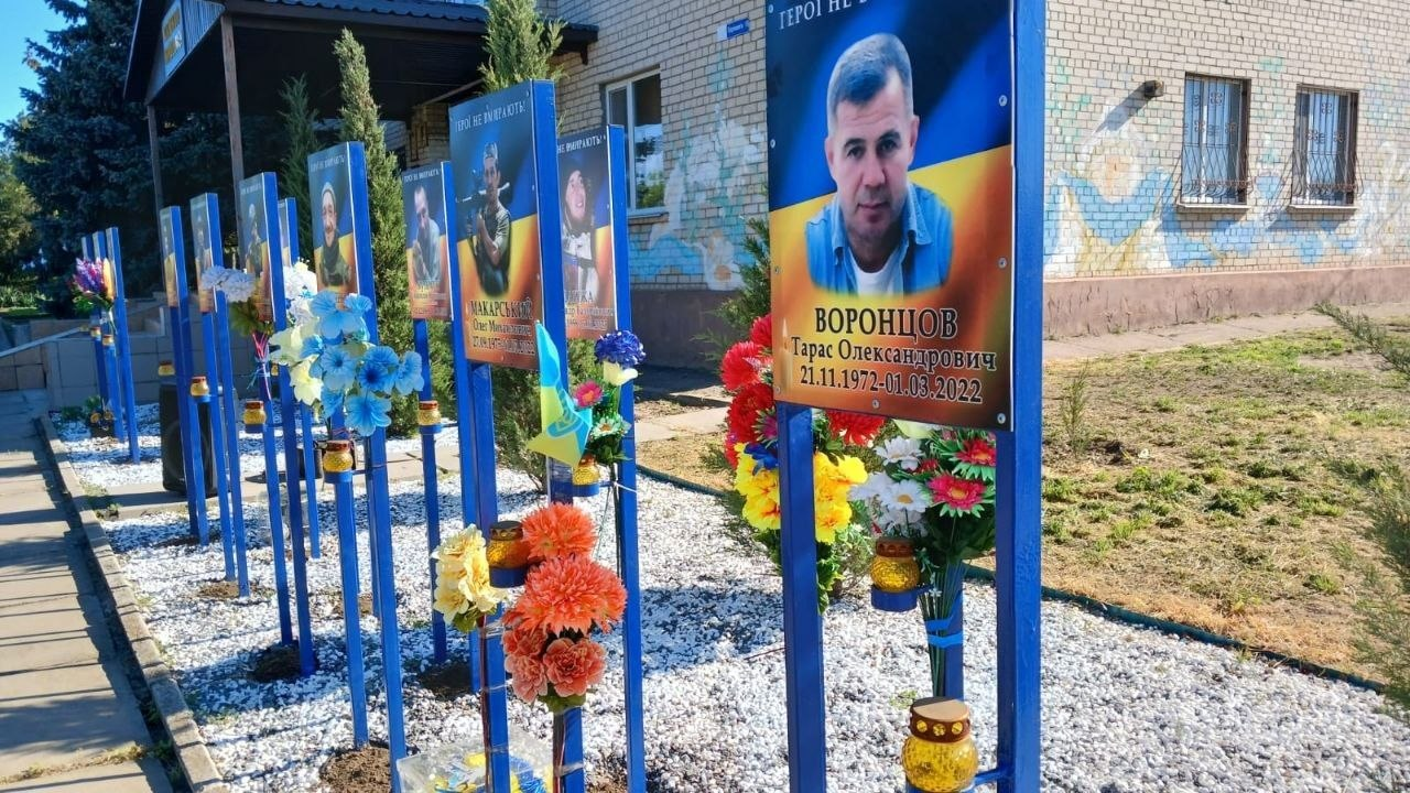 Алея пам'яті з портретами загиблих захисників на синьо-жовтому фоні, встановленими вздовж доріжки. Біля кожного стенда розміщені квіти, лампадки та маленькі державні прапори.