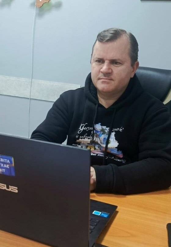 Чоловік у чорному худі з принтом сидить за дерев'яним столом у робочому кабінеті та дивиться на екран відкритого ноутбука ASUS.