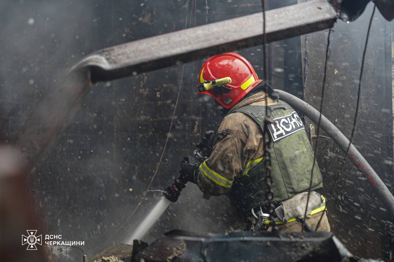 Рятувальник у захисній формі з написом «ДСНС» та яскраво-червоному шоломі ліквідовує загоряння всередині сильно задимленого приміщення. Він тримає пожежний ствол, з якого б'є потужний струмінь води. У лівому нижньому кутку розміщено логотип ДСНС Черкащини.