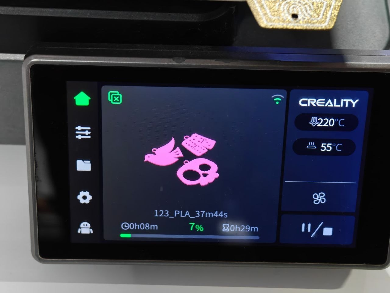 Дисплей 3D-принтера бренду Creality відображає процес друку моделі з філаменту типу PLA. На екрані видно рожеві силуети силуету птаха, емблеми та черепа, а також технічні параметри: температура сопла 220°C, температура столу 55°C та прогрес виконання на рівні 7%.