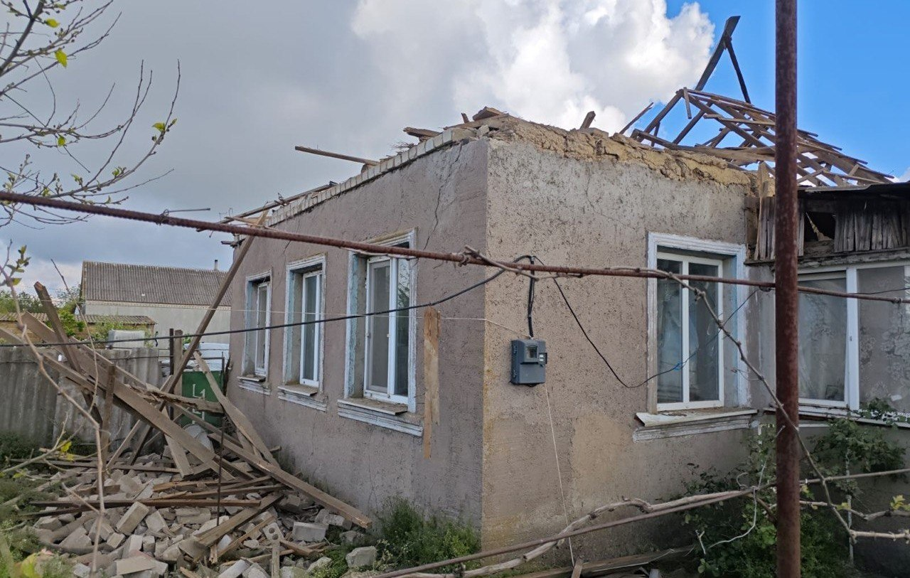 Одноповерховий житловий будинок із суттєвими руйнуваннями після обстрілу. У будівлі повністю знищено дах, оголено дерев'яні крокви, а ліворуч на землі лежить купа уламків будматеріалів, цегли та дощок на тлі хмарного неба.