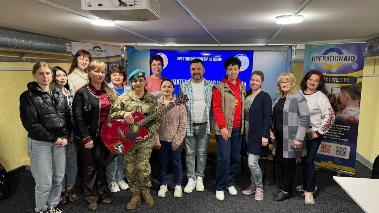 Група людей стоїть разом у приміщенні на тлі великого екрана з написом «Креативний простір 