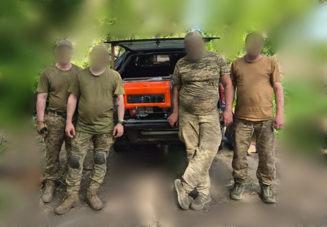 Чотири чоловіки у військовій формі та футболках позують біля відчиненого багажника автомобіля, в якому стоїть новий помаранчевий генератор.
