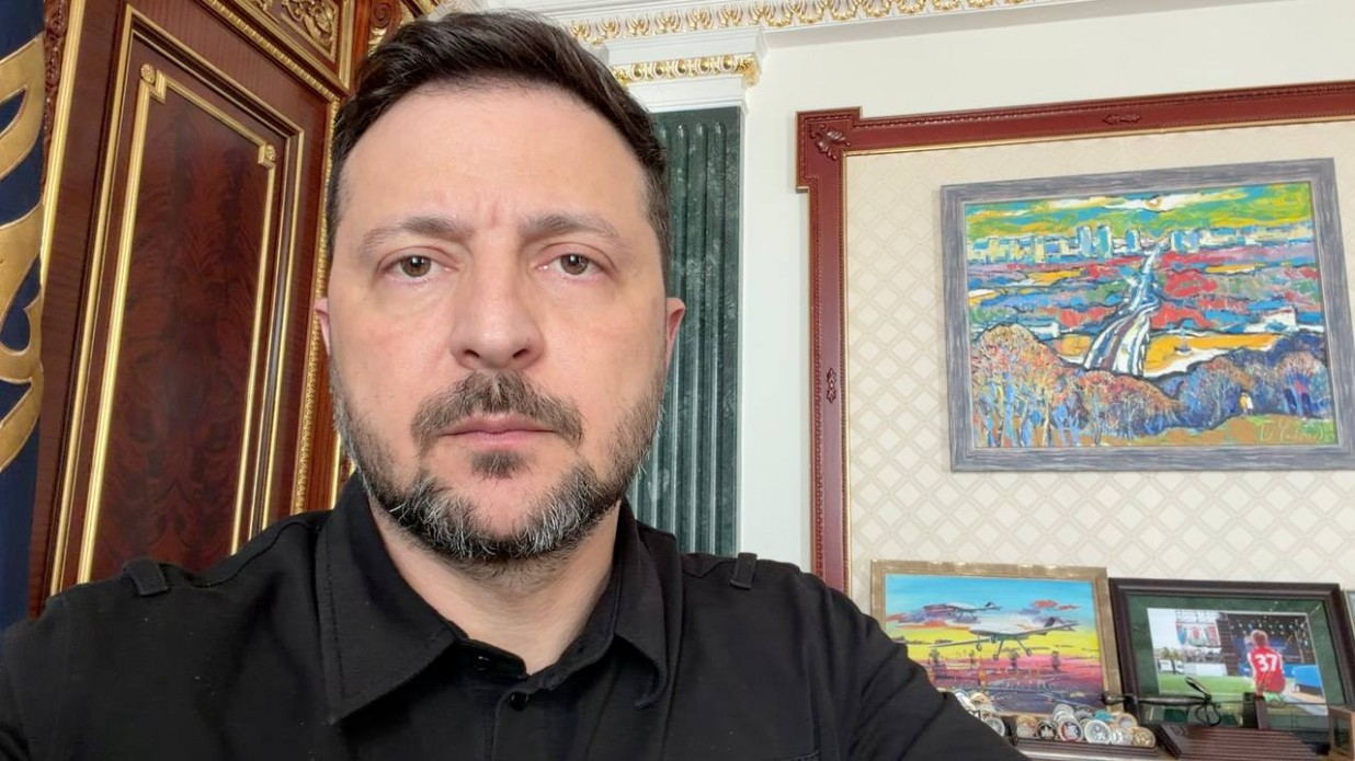Чоловік із короткою стрижкою та бородою сидить у робочому кабінеті, на стіні позаду нього висить яскрава картина із міським пейзажем.