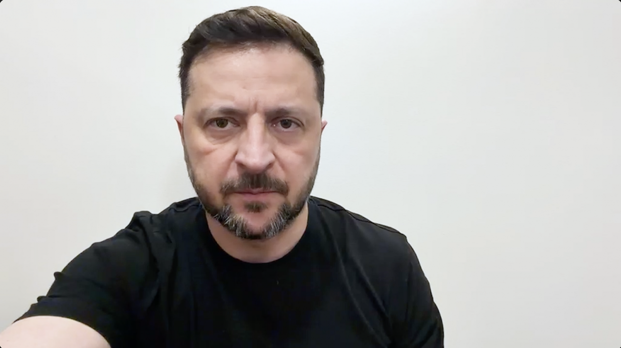 Чоловік із короткою темною стрижкою та бородою дивиться прямо в камеру. Він одягнений у чорну футболку, а позаду нього розташована однотонна світла стіна.