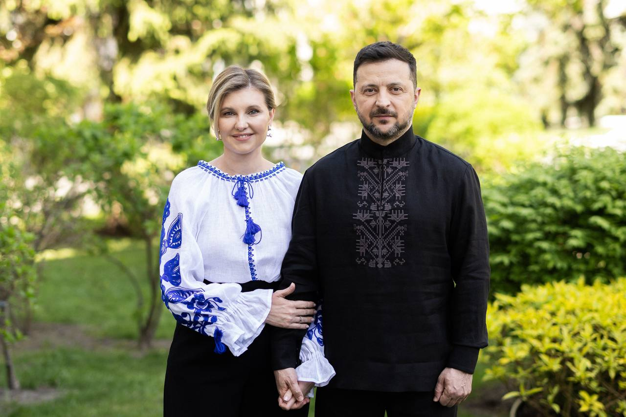 Спільне фото чоловіка та жінки на повний зріст, які тримаються за руки на тлі зеленого саду. Вони вбрані у традиційні українські вишиванки: жінка у білу сорочку з синім орнаментом, а чоловік — у чорну сорочку з вишитим візерунком у тон.