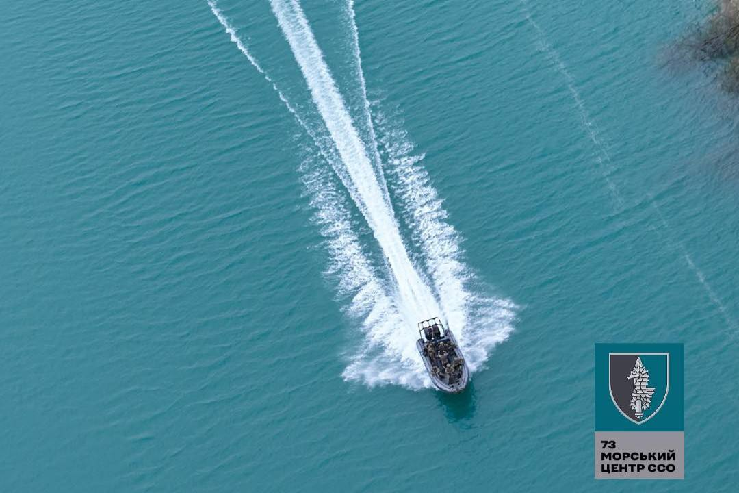 Швидкісний військовий човен із групою бійців на борту рухається по водній поверхні, залишаючи за собою білий пінистий слід. У правому нижньому кутку розміщено емблему 73-го морського центру ССО.