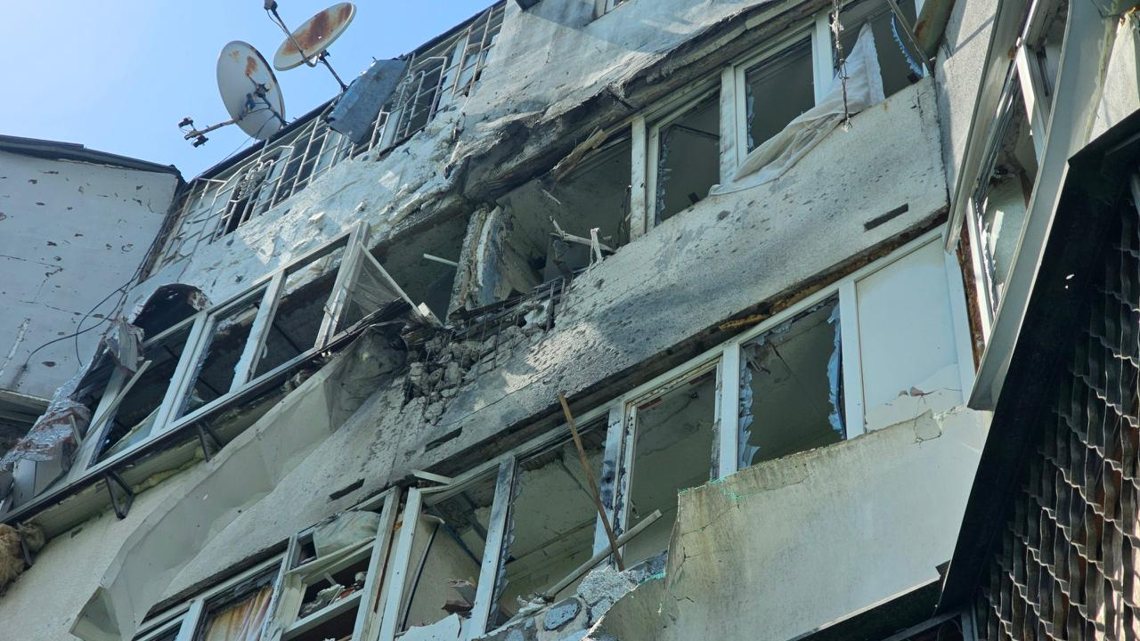 Зруйнований обстрілом багатоповерховий житловий будинок із вибитими вікнами, пошкодженими балконами та посіченими уламками стінами на тлі неба.