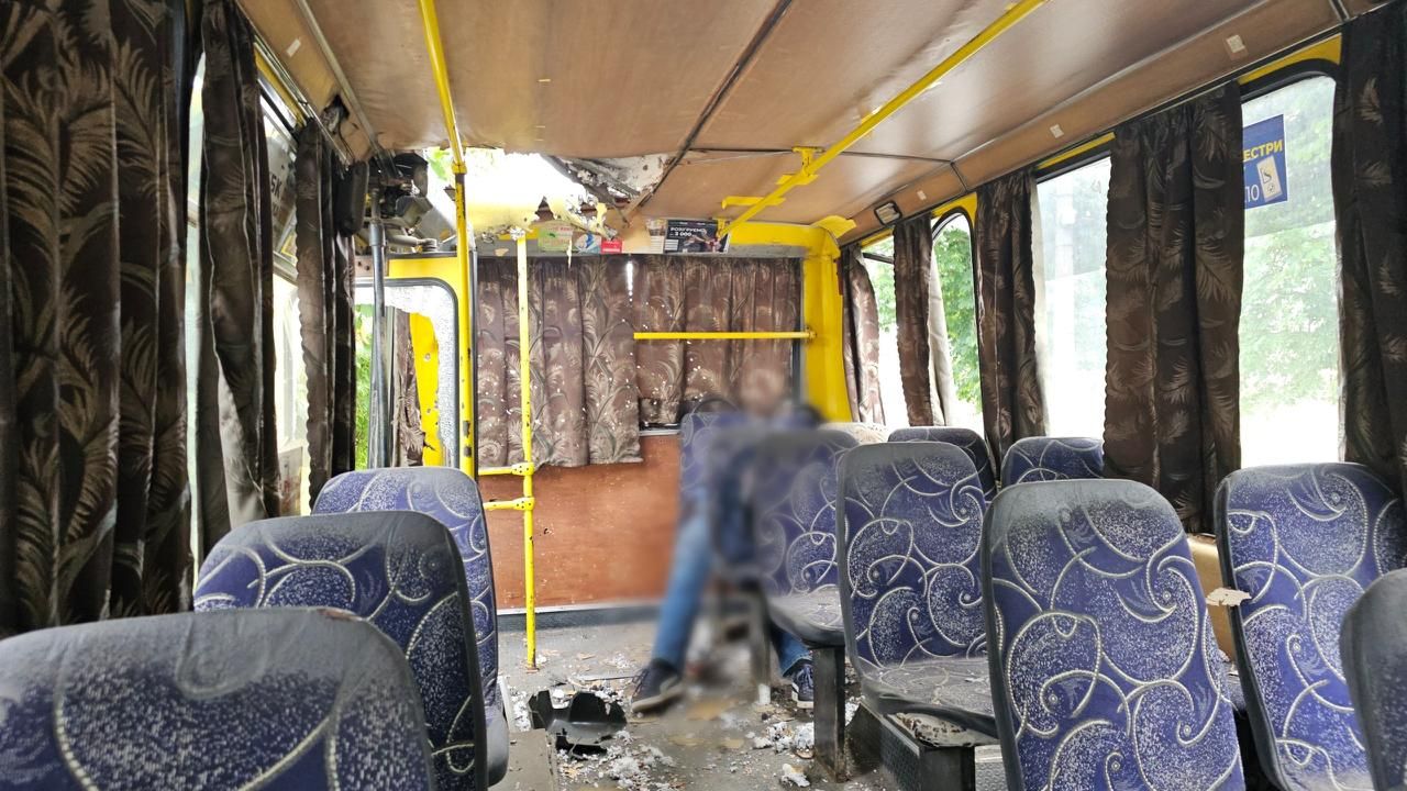 Салон маршрутного автобуса з пасажирськими сидіннями, посіченими шторами, уламками на підлозі та сильно пошкодженою передньою частиною даху.
