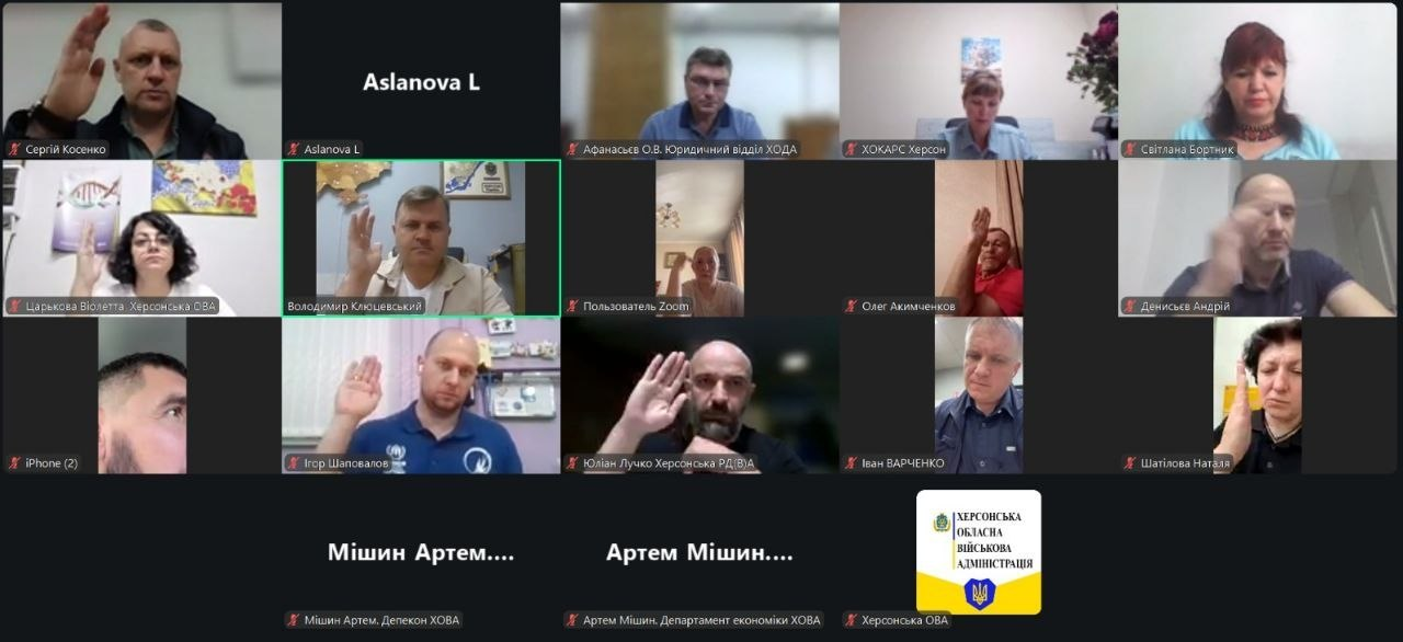 Скриншот онлайн-наради у Zoom, де більшість учасників на своїх відеовікнах тримають підняту руку для голосування, а внизу відображається логотип Херсонської обласної військової адміністрації.