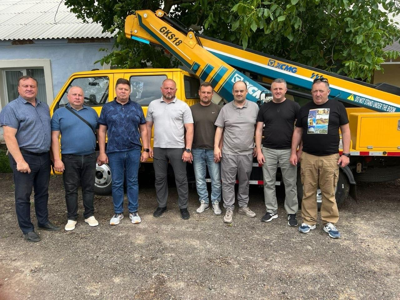 Група з восьми чоловіків стоїть у ряд на вулиці біля великого жовтого автомобіля-автовишки марки XCMG з підйомною стрілою моделі GKS18.
