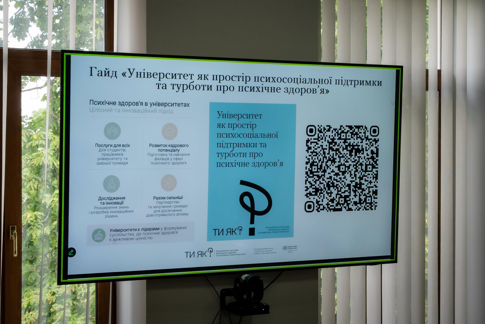 Екран монітора у приміщенні, на якому демонструється презентація гайду «Університет як простір психосоціальної підтримки та турботи про психічне здоров’я» із QR-кодом та логотипами програми «Ти як?».
