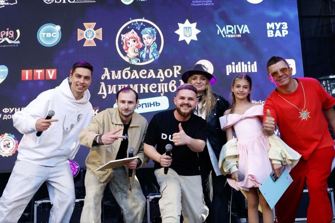 Група людей позиціонує для фото на сцені на тлі великого екрана з логотипами та написом «Амбасадор Дитинства».