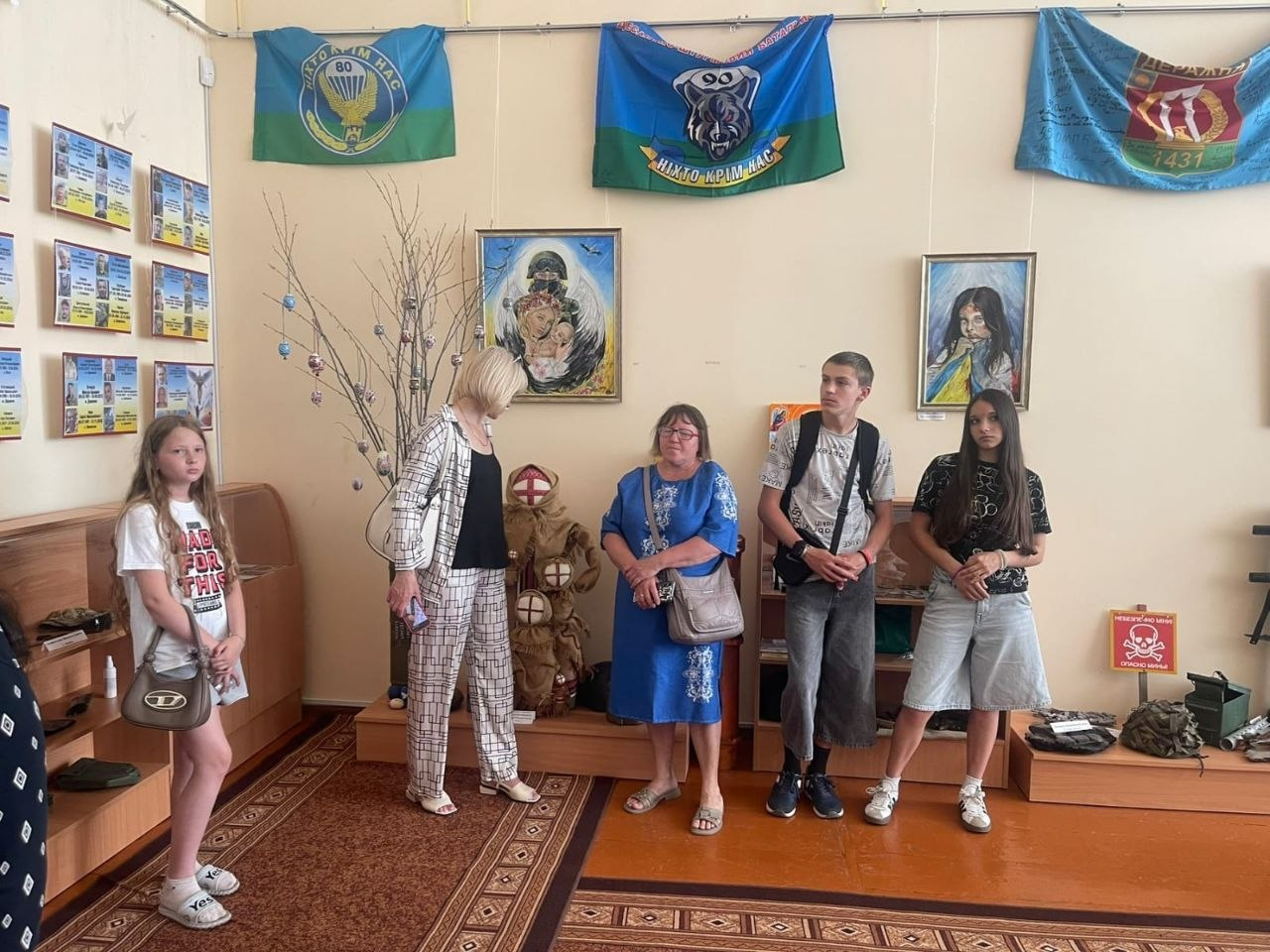 Група людей розглядає експонати в музейній кімнаті, на стінах якої розвішані прапори, картини та інформаційні стенди.