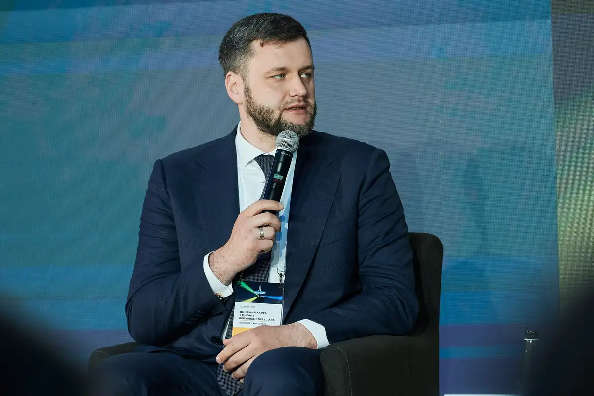 Чоловік у діловому костюмі та з мікрофоном у руці виступає під час конференції.
