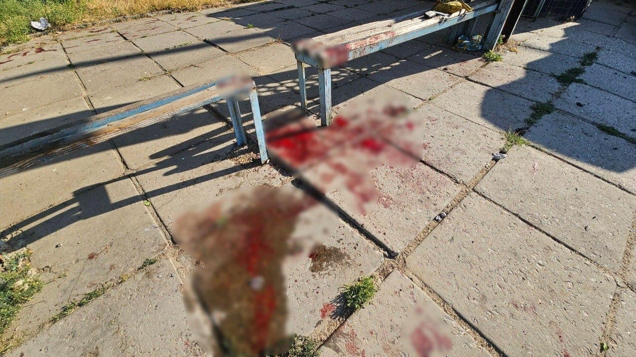 Зупинка громадського транспорту з бетонним покриттям, лавками та численними слідами крові на плитах.