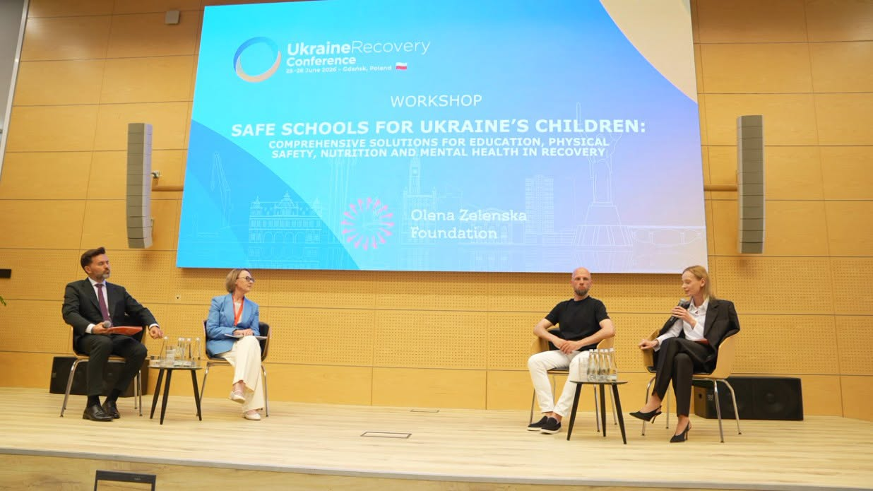 Спікери під час панельної дискусії на сцені конференції «Ukraine Recovery Conference» перед великим екраном із текстом про безпеку українських дітей.