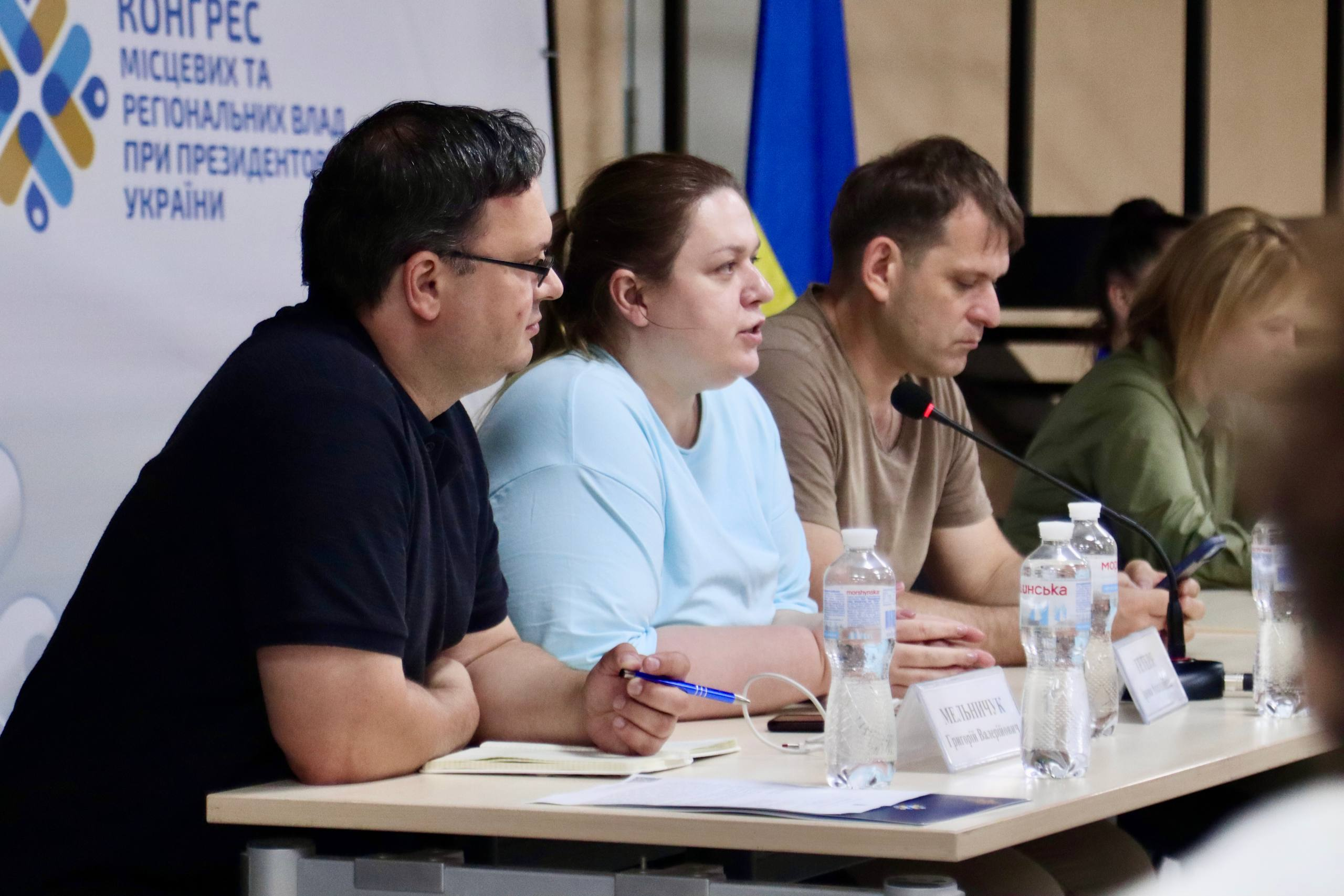 Чотири людини сидять за довгим столом на тлі офіційного банера з написом «Конгрес місцевих та регіональних влад при Президентові України», перед ними стоять пляшки з водою та таблички.