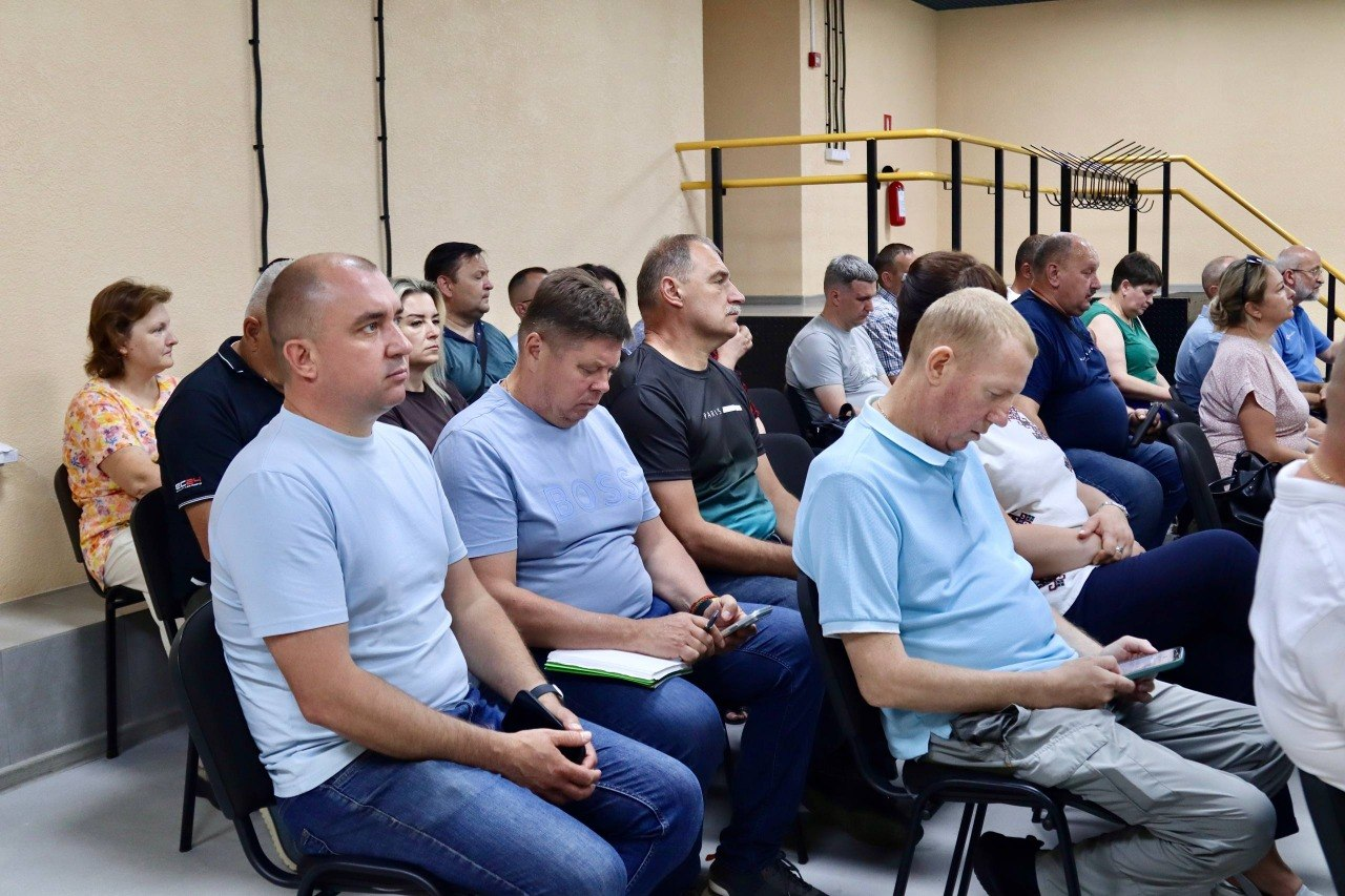 Група людей сидить рядами на стільцях у великій залі під час офіційних зборів або конференції. Більшість присутніх зосереджено дивляться вперед, дехто тримає в руках телефони чи блокноти.