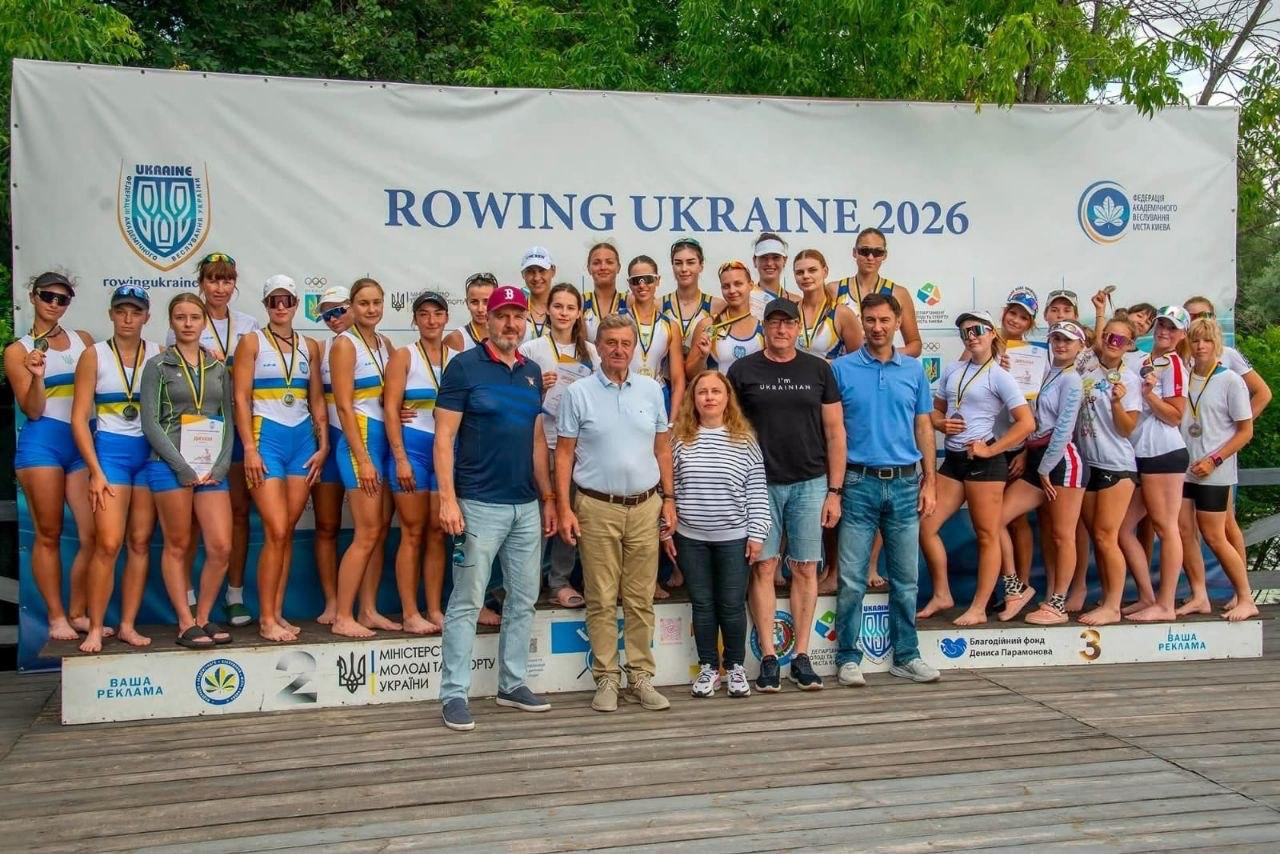 Велика група спортсменок та офіційних осіб позує для спільного фото на тлі банера «Rowing Ukraine 2026» під час церемонії нагородження.