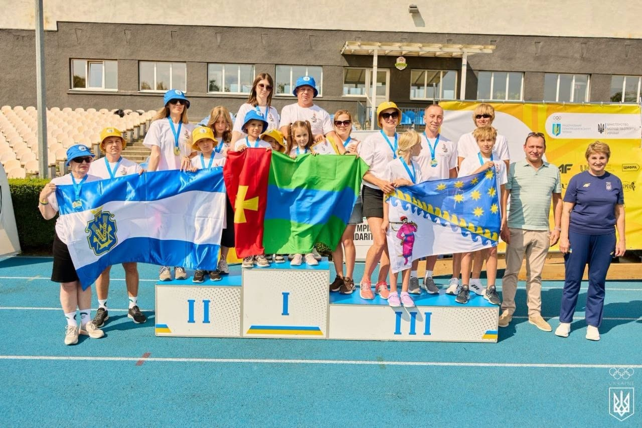 Церемонія нагородження на стадіоні, де призери змагань із медалями стоять на трирівневому п'єдесталі та тримають прапори своїх команд на тлі трибун.