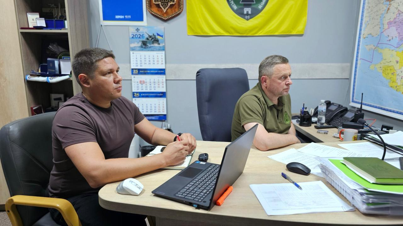 Двоє чоловіків сидять за робочим столом в офісному кабінеті перед ноутбуком і документами.