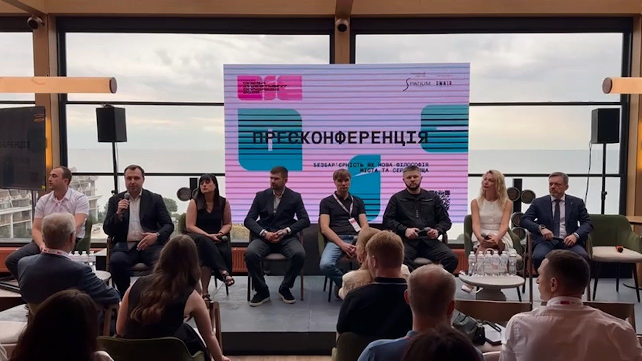 Прес-конференція на тему «Безбар'єрність як нова філософія міста та сервісу» в межах Odesa Investment Forum 2024. Вісім спікерів сидять у президії на тлі великого екрана з назвою події та панорамного вікна з видом на море, а перед ними на стільцях розмістилися слухачі в залі.