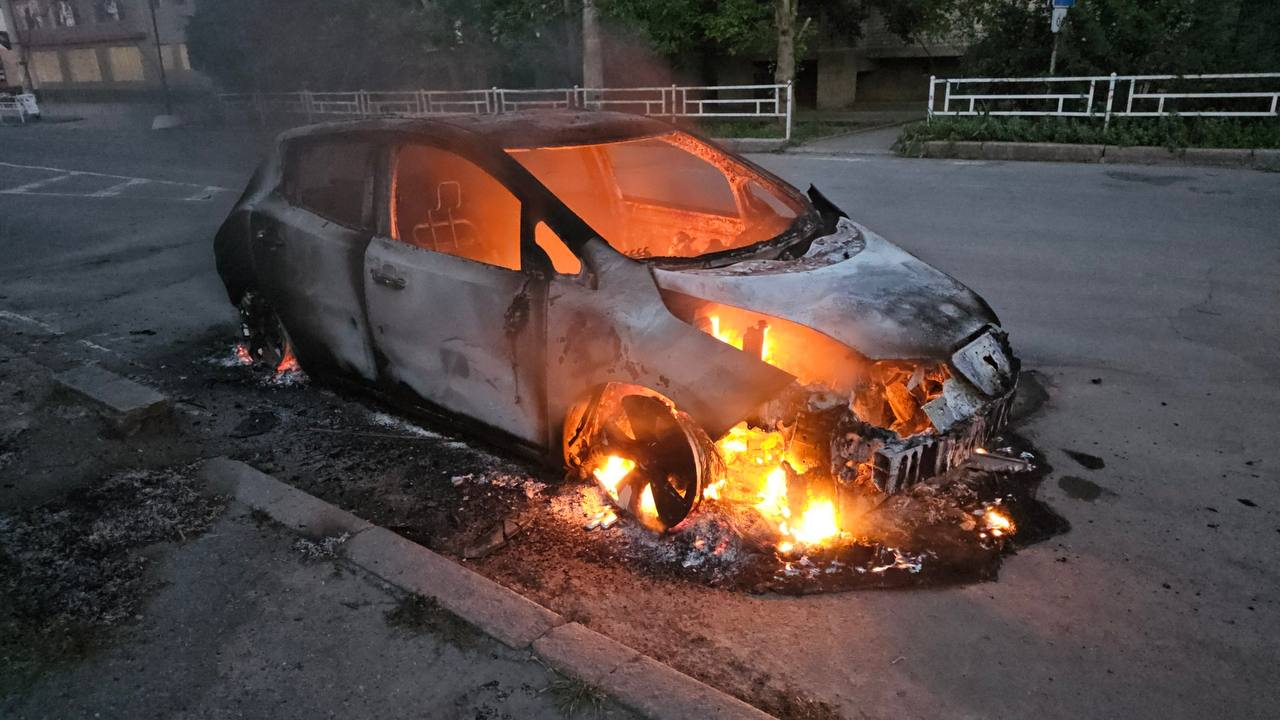 Легковий автомобіль повністю охоплений вогнем на узбіччі міської дороги в сутінках.