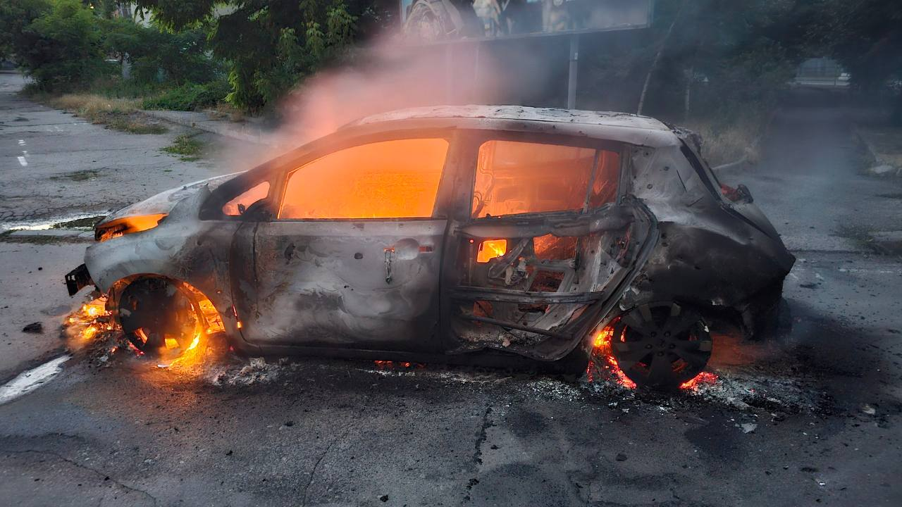 Легковий автомобіль із сильно пошкодженим кузовом горить зсередини на асфальтованій дорозі, випускаючи дим та яскраве полум'я через вікна.