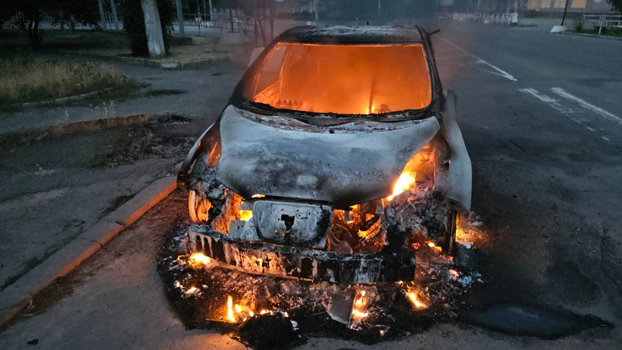 Легковий автомобіль з обгорілою передньою частиною горить посеред дороги, а його салон повністю охоплений яскравим полум'ям.