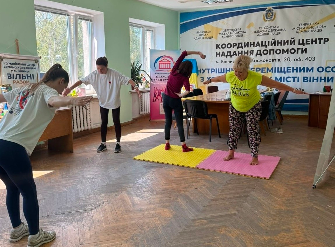 Група жінок займається фізичною руханкою у світлому приміщенні координаційного центру надання допомоги.