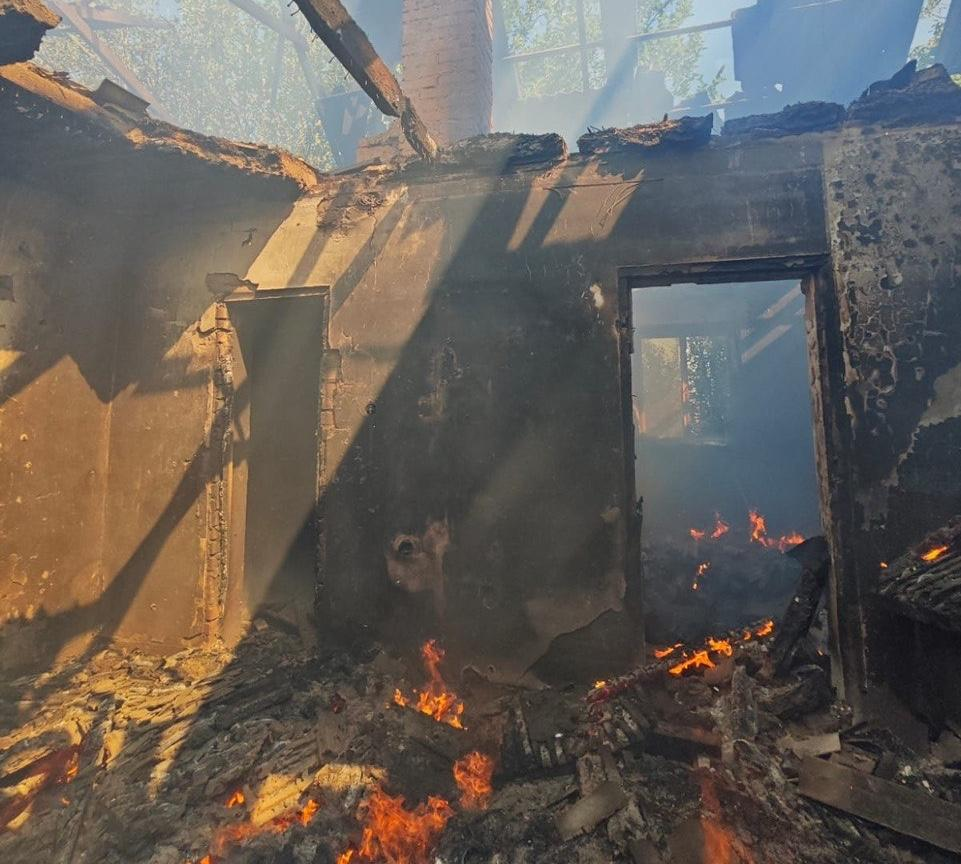 Зруйнована пожежею будівля із повністю згорілим дахом та обвугленими стінами, де на підлозі та в дверних проємах продовжує палати відкритий вогонь, утворюючи задимлення.
