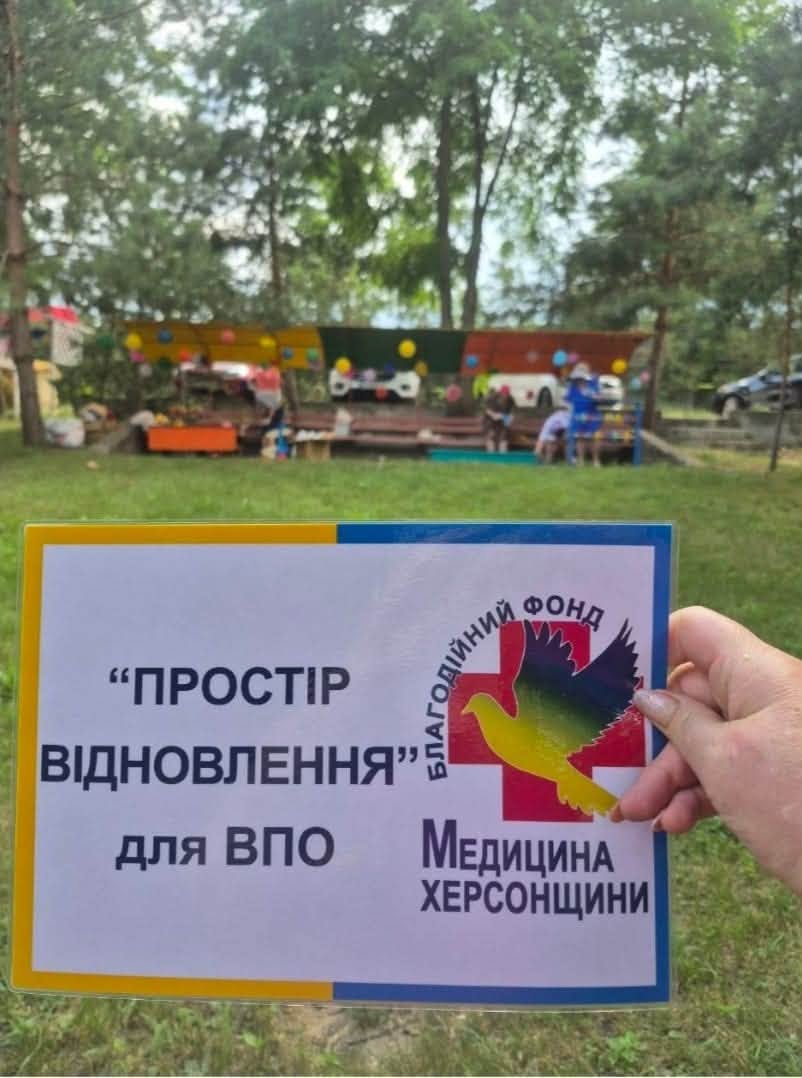 Рука людини тримає інформаційну табличку в синьо-жовтій рамці з текстом «