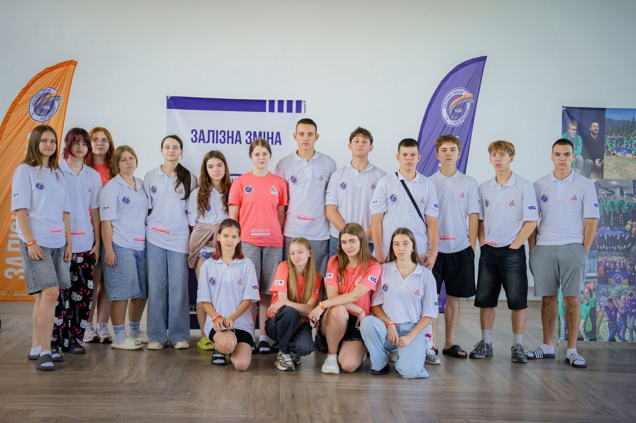 Група підлітків-учасників проєкту «Залізна зміна» у фірмових футболках позує для спільного фото у приміщенні.
