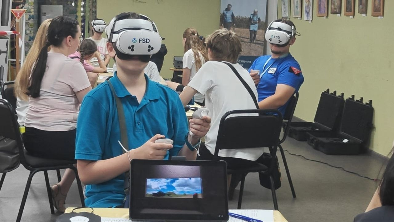 Підлітки та дорослі учасники інтерактивної VR-сесії з мінної небезпеки в координаційному центрі «Вільні разом» у Дніпрі тестують симуляції за допомогою окулярів віртуальної реальності та контролерів від команди FSD в Україні.