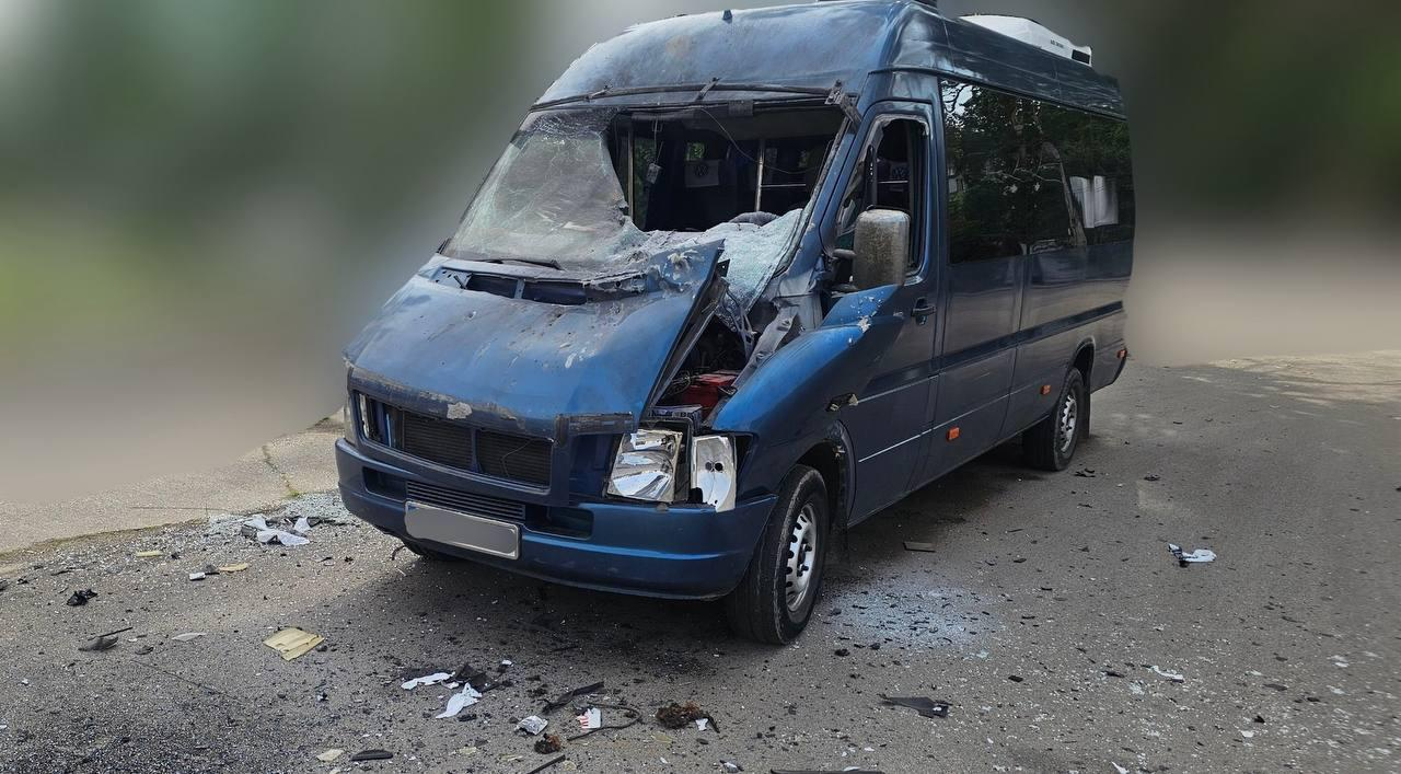 Сильно пошкоджений внаслідок обстрілу або ДТП синій мікроавтобус із розбитим лобовим склом, зім'ятим капотом та уламками на асфальті навколо.