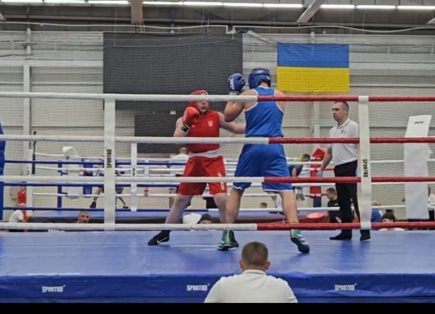 Боксер у червоній формі та боксер у синій формі ведуть поєдинок на ринзі під наглядом рефері під час Чемпіонату України серед юніорів в Ужгороді.