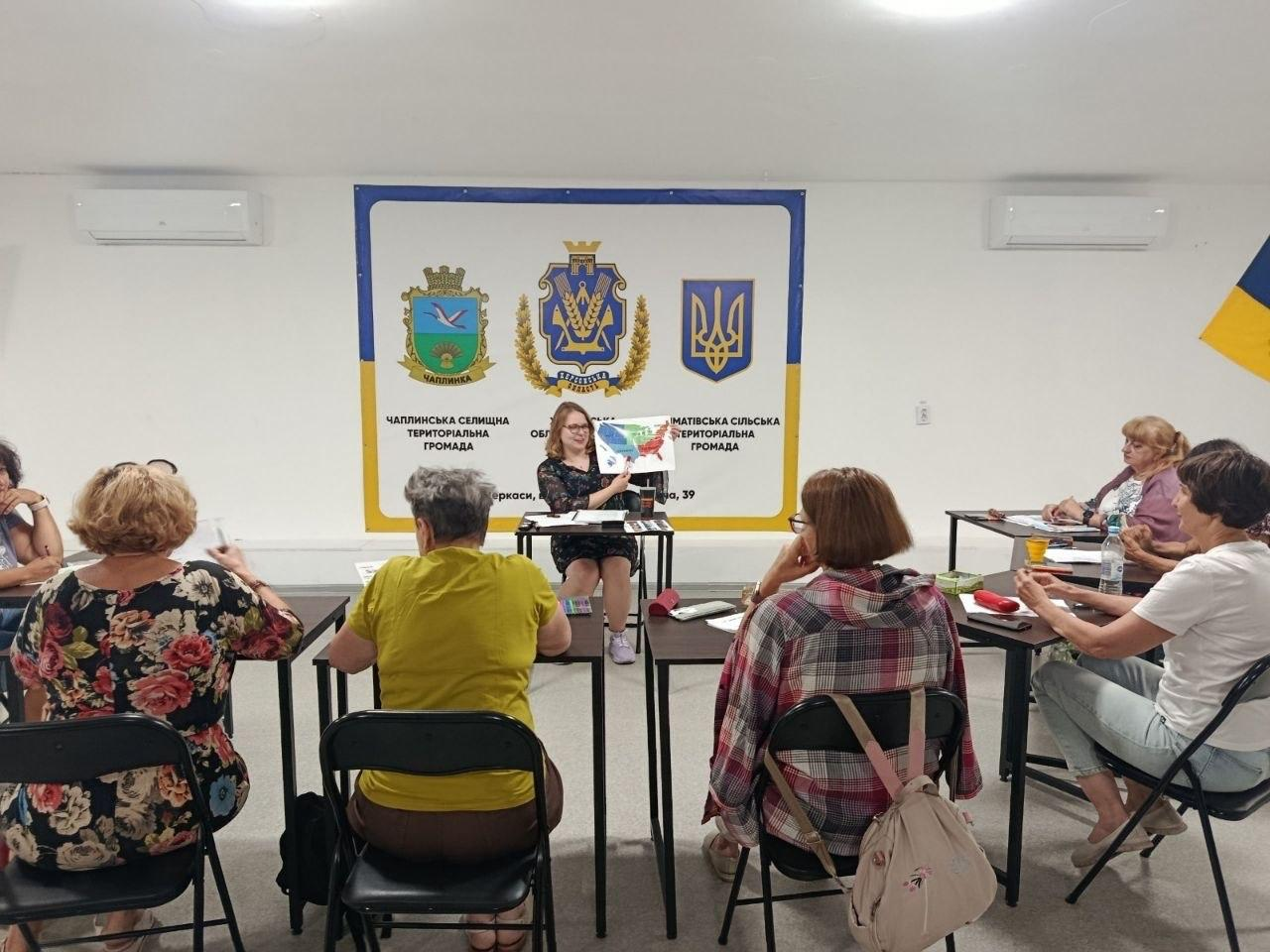 Волонтерка з Херсонщини проводить заняття з англійської мови, присвячене культурологічним особливостям США, демонструючи учасницям карту американських штатів та розповідаючи про регіональні традиції й стиль життя.