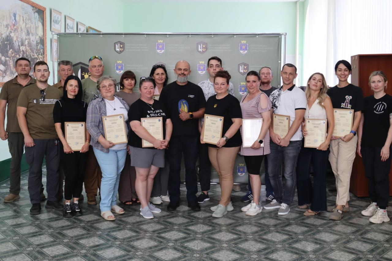 Групове фото учасників 23-ї групи фахівців Херсонської ОВА та громад області з отриманими свідоцтвами в руках після успішного завершення курсу базової військової підготовки на базі Миколаївського обласного центру підготовки громадян до національного спротиву.