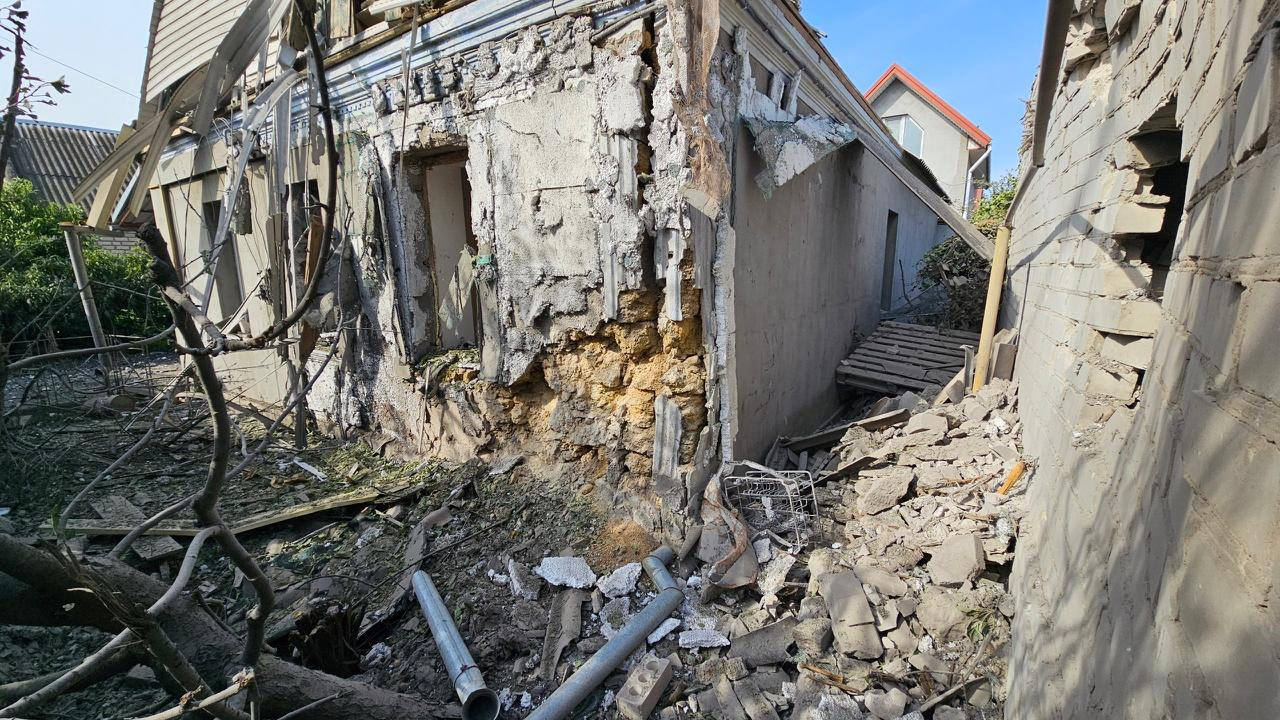 Зруйнований обстрілом одноповерховий житловий будинок із пошкодженим фасадом, осипаною кам'яною кладкою та купами будівельного сміття на землі.