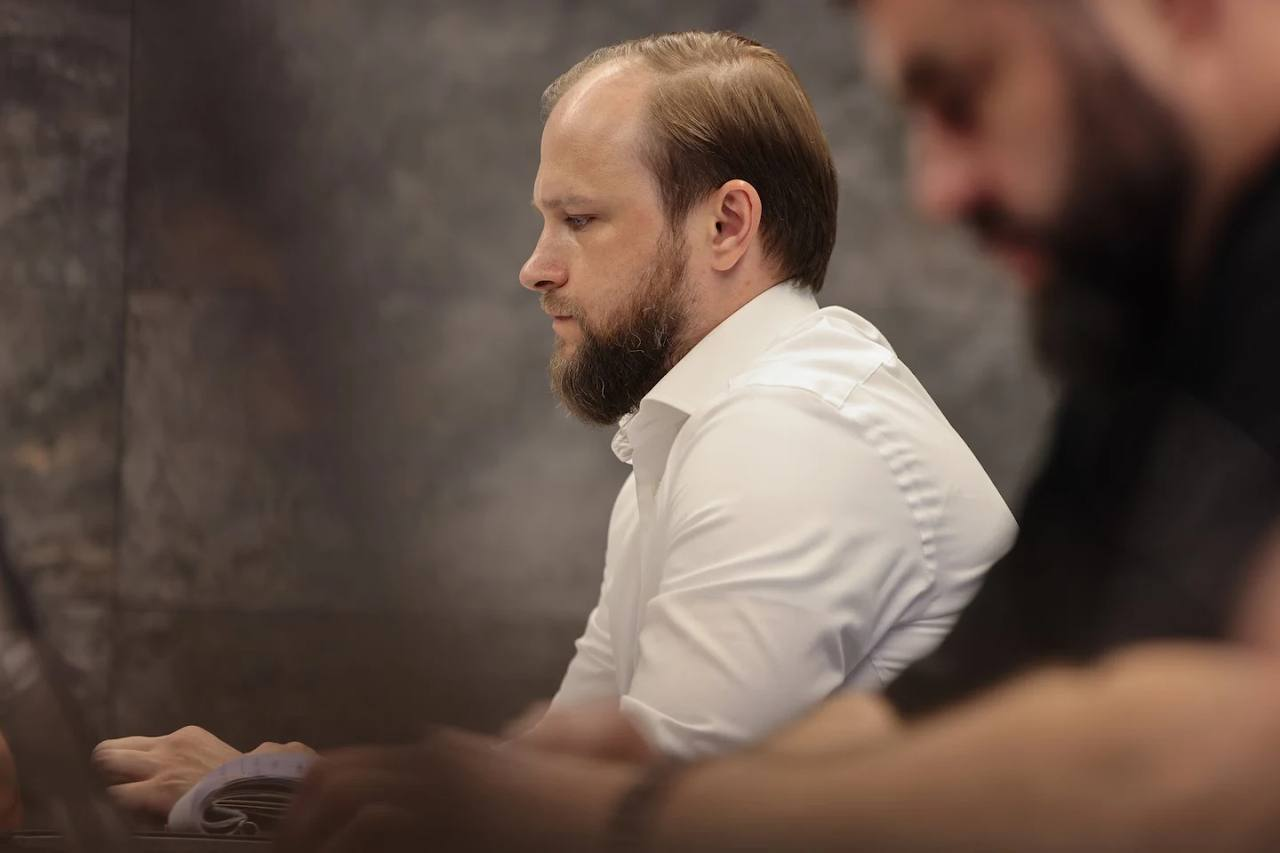 Учасник наради з боку профілю у білій сорочці працює за ноутбуком під час обговорення енергетичної стійкості регіонів.